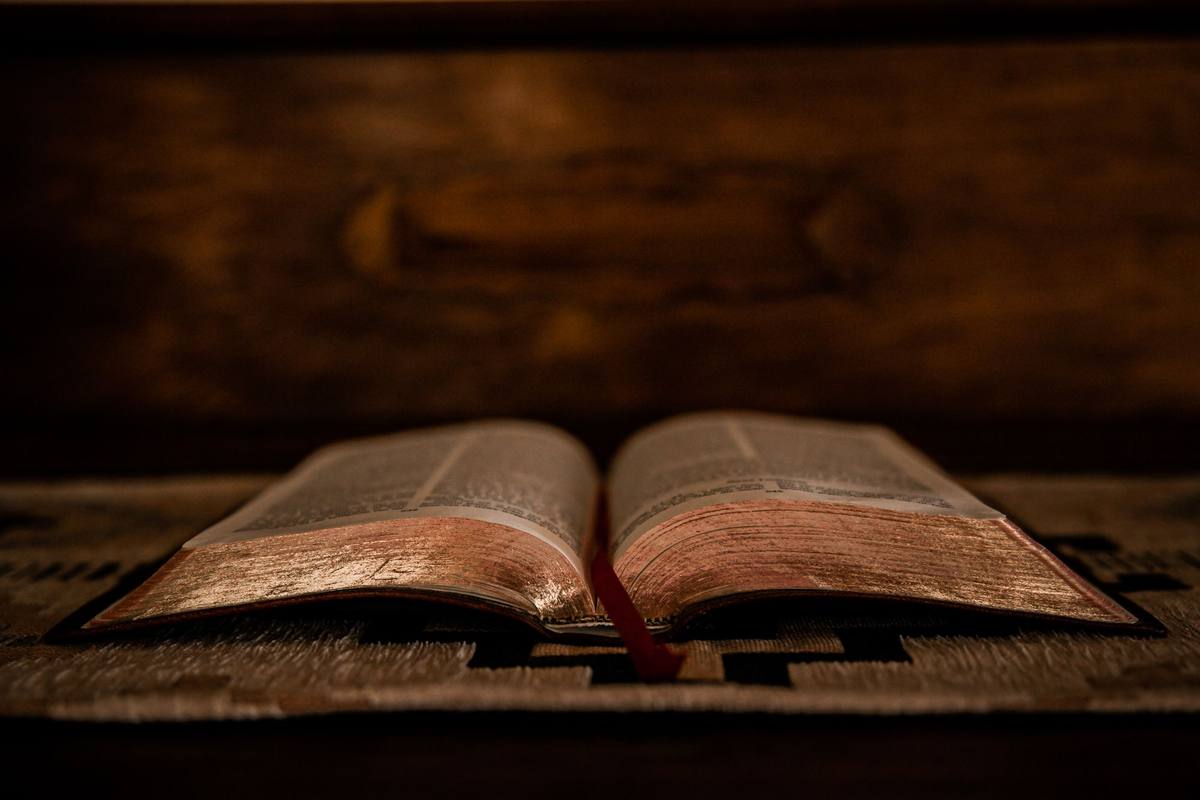 An open Bible lying on dark wood in warm, low light.